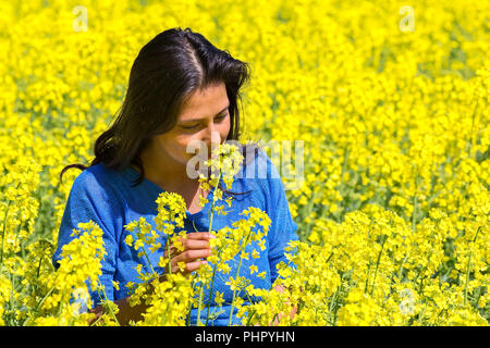 Woman smells flower in yellow rapeseed field Stock Photo