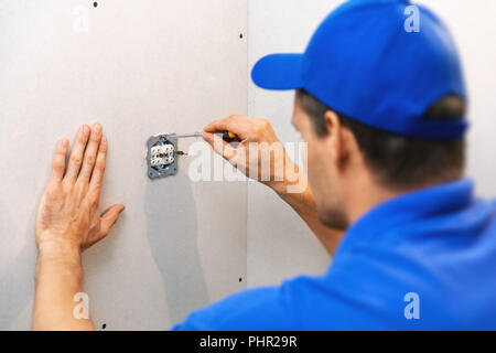 electrician installing electrical outlet on the wall Stock Photo