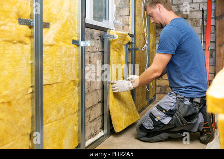 old house reconstruction - construction worker insulating brick wall with glass wool Stock Photo