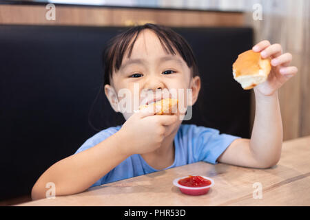 Asian Chinese little girl eating fried chicken at indoor restaurant Stock Photo