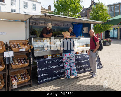 A man and a woman chatting with stallholders on the Little Yorkshire Cheese stall in Ripon Market North Yorkshire England UK Stock Photo
