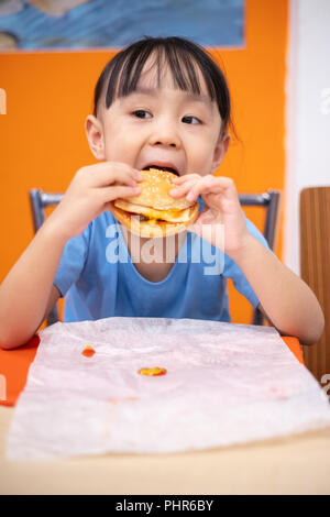 Asian Chinese little girl eating burger at indoor restaurant Stock Photo