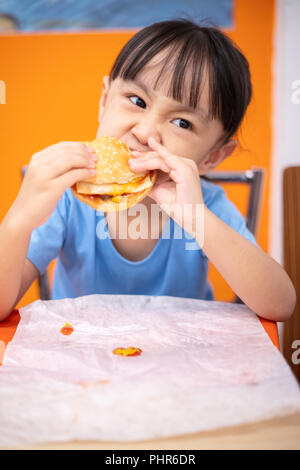 Asian Chinese little girl eating burger at indoor restaurant Stock Photo