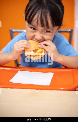 Asian Chinese little girl eating burger at indoor restaurant Stock Photo