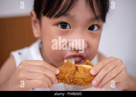 Asian Chinese little girl eating fried chicken at indoor restaurant Stock Photo