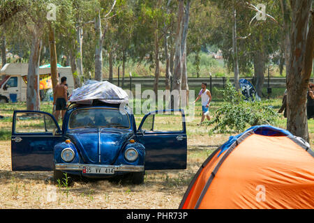 A classic blue VW Beetle parked up in the shade with the doors open on a hot sunny day on a camp site with campers in the background. Stock Photo