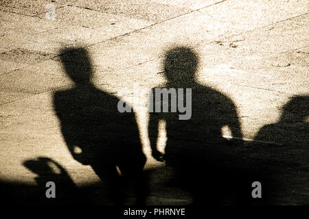 Shadows silhouettes of group of men standing on summer promenade in sepia black and white Stock Photo