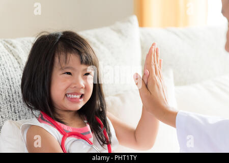 Happy little cute girl on consultation at the pediatrician. Girl is smiling and giving high five to doctor. Medicine and health care concept. Stock Photo
