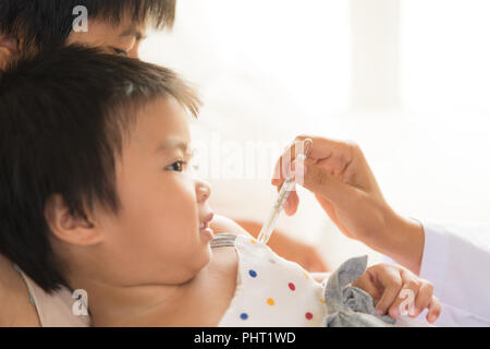 Doctor holding digital thermometer to measuring temperature of her ill kid and sick little girl with mother. Stock Photo