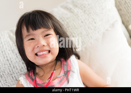 Cute little girl is smiling and playing doctor with stethoscope. Kid and health care concept. Stock Photo