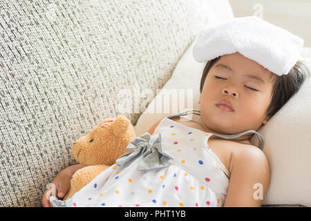 Young little girl sleeping and sick on the sofa with cooler gel on her head and measuring temperature by thermometer. and take care by her mom. Stock Photo