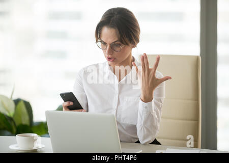 Angry businesswoman annoyed with stuck not working phone in offi Stock Photo