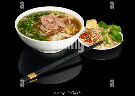 Plate of vietnamese noodle soup Pho Bo isolated on black reflecting background. Served with chopsticks, soybean sprouts and chili. Stock Photo