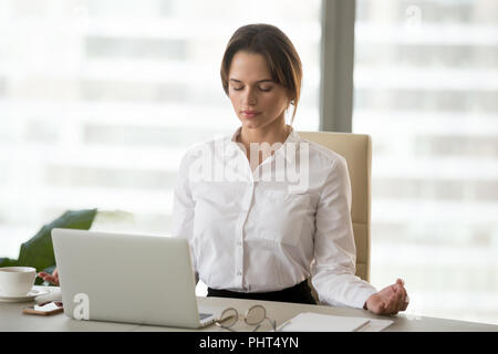 Mindful millennial woman meditating in office to reduce work str Stock Photo