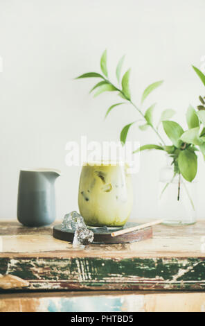 Iced matcha latte drink in glass, white wall and plant branches at background, copy space. Summer refreshing beverage cold drink Stock Photo