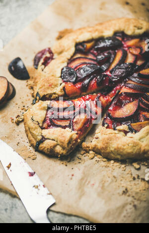 Plum galetta sweet cake on baking paper over grey concrete background, selective focus. Seasonal Fall or Autumn dessert Stock Photo