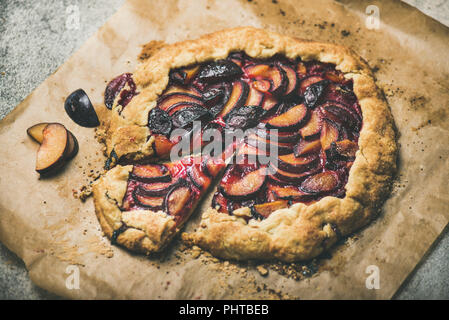 Round plum galetta sweet cake on baking paper over grey concrete background, selective focus, horizontal composition. Seasonal Fall or Autumn dessert Stock Photo