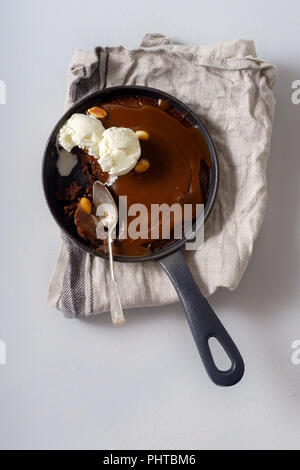 Brownie in a skillet with a scoop of vanilla ice cream, salted caramel and roasted peanuts Stock Photo