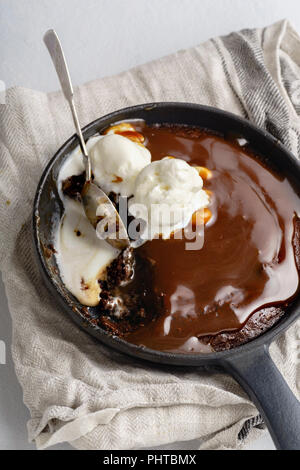 Brownie in a skillet with a scoop of vanilla ice cream, salted caramel and roasted peanuts Stock Photo