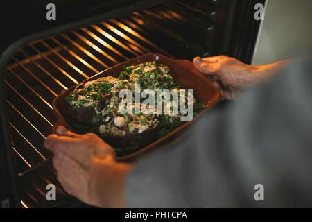 A person placing a tray of artichokes in to the oven to bake. Stock Photo
