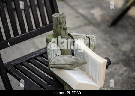 Wooden figure sat on a garden chair outside reading a book Stock Photo