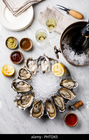 Open Oysters with lemon, sauce and Champagne in ice bucket on white marble background Stock Photo