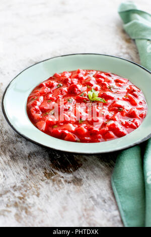 Strawberry Basil Jam served in a enamel bowl. Photographed on a rustic white background.
