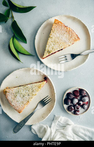 Cherry pie slices served on two white plates with forks on the side on grey background photographed from top view. Green leaves and cherries dusted wi Stock Photo