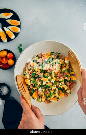 Hands stirring potato tuna egg salad in a ceramic bowl using wooden spoons. Stock Photo