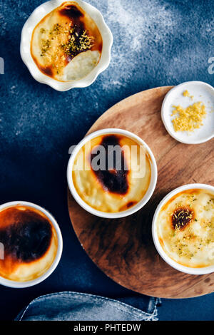 Baked rice pudding in white ramekins served on a wooden board photographed on a dark background from top view. Stock Photo