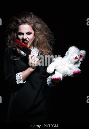 Horror shot: a scary demonic girl with torn rabbit toy and bloody knife in hands Stock Photo