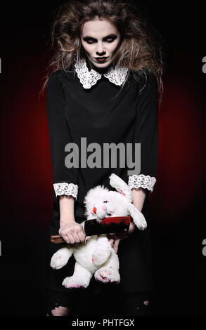 Horror shot: a scary wicked girl with rabbit toy and bloody knife in hands Stock Photo