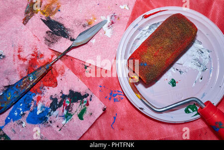 Colorful roller lying on the white plate with a palette knife after beign used by a professional artist for wall art painting, top angle, colorful pin Stock Photo