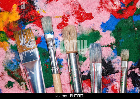 Five worn out brushes of different sizes on the messy colorful pink palette artistic background Stock Photo