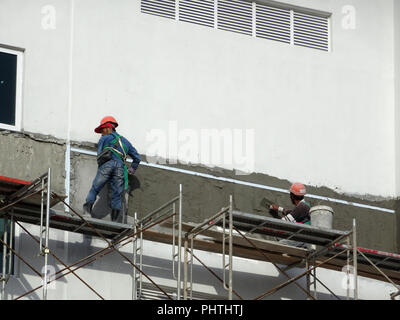 Construction workers plastering wall using cement plaster at the construction site. They are wearing appropriate safety gear to prevent bad happen Stock Photo