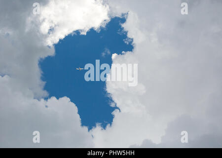 An airliner at high altitude passes through an opening in thick, threatening clouds. Stock Photo