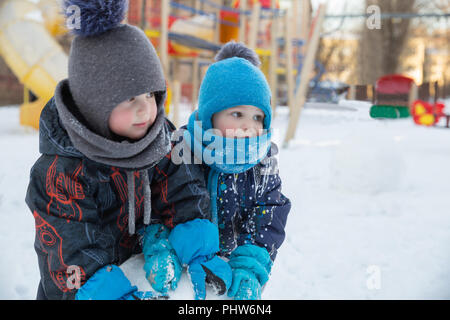 Two cute children boys in warm clothes in winter play in playground Stock Photo