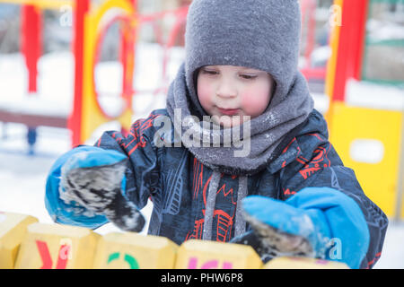 Serious boy 4 years in winter on playground playing dice with  letters Stock Photo