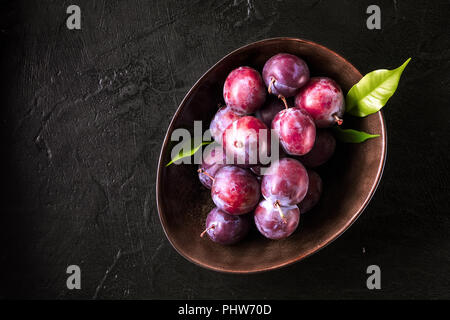 Whole fresh red violet blue plums and slices cut with knife in bowl on kitchen table Stock Photo