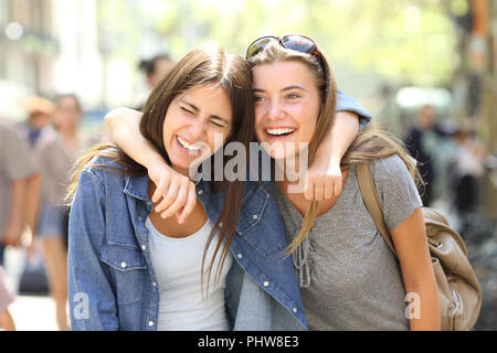 Two funny friends laughing loud walking in the street Stock Photo