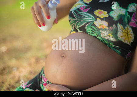 Pregnant woman in a park putting cream on her belly to avoid stretch marks.