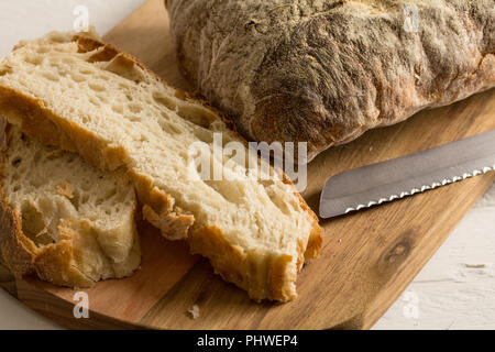 Bread and slices with bread knife on wooden bread board close up Stock Photo