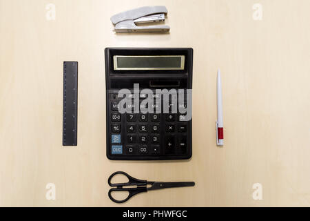 A set of office tools consisting of a calculator, pen, stapler, ruler and scissors lying on a light colored wooden table Stock Photo