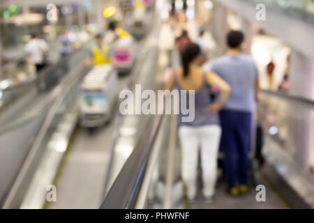 Tourist couple standing on escalator in international airport in motion blur. Stock Photo