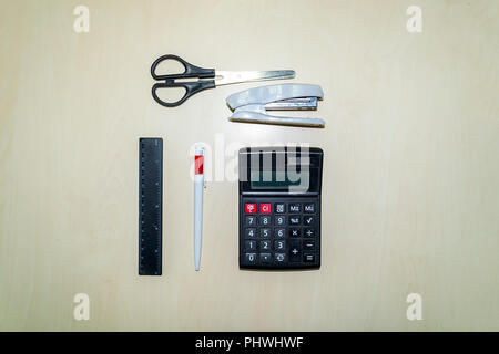 A set of office tools consisting of a calculator, pen, stapler, ruler and scissors lying on a light colored wooden table Stock Photo