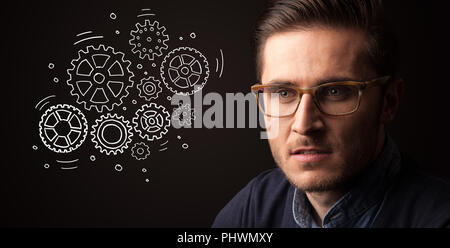Portrait of a young businessman with rotating gears next to him on a dark background Stock Photo