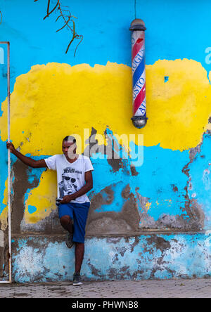 Anholan young man standing in front of a barber shop pole sign, Benguela Province, Benguela, Angola Stock Photo