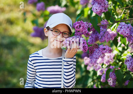 Smiling little girl smelling lilacs in the garden. Beautiful spring day. Selective focus. Stock Photo