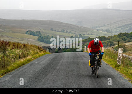 Cyclist pedals on after cycling up a very steep hill in the Yorkshire Dales national park, UK Stock Photo
