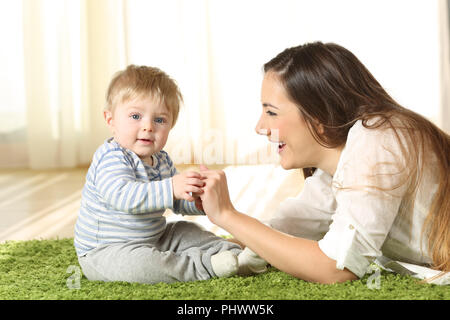 Mother playing with her kid that looks at camera on the floor at home Stock Photo